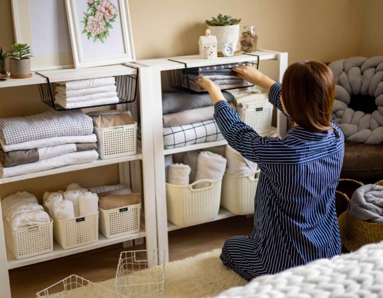 Domestic woman in pajamas neatly putting folded linens into cupboard vertical storage Marie Kondo